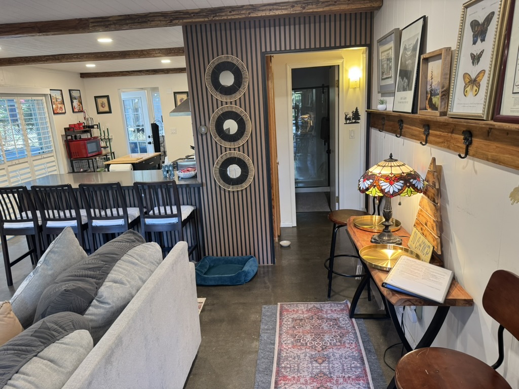 Open dining area with a long breakfast bar, six stools, entry coat hooks and framed botanical prints