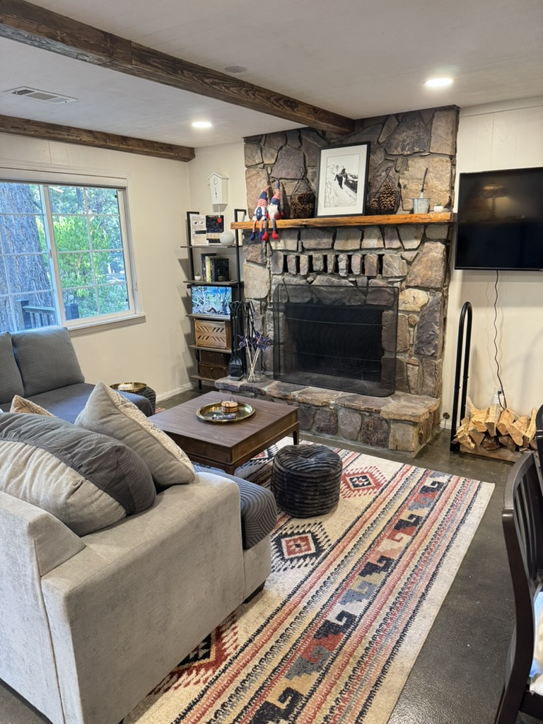 Cottage living room with a floor-to-ceiling stone fireplace, exposed timber beams, deep sectional sofa, kilim rug and a wall-mounted television